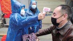 A health worker takes a body temperature measurement of a man at the entrance to a residential compound in Wuhan.