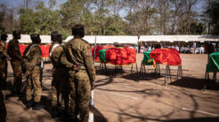 Des responsables militaires se tiennent à côté de cercueils recouverts de drapeaux nationaux du Burkina Faso à Ouagadougou le 23 février 2023, avant la cérémonie de réinhumation de la dépouille de Thomas Sankara aux côtés de ses douze compagnons, tués le 15 octobre 1987.