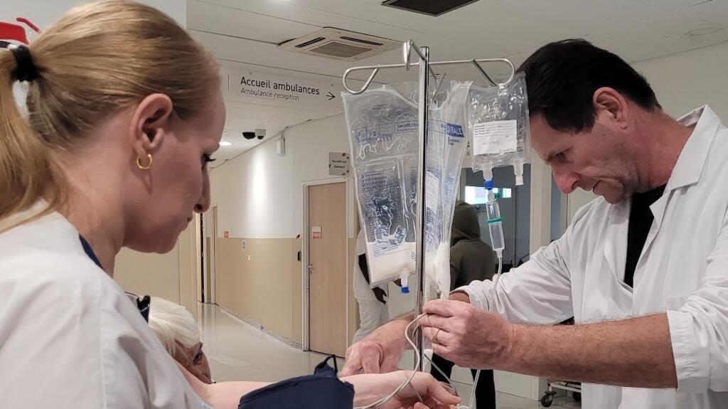 O responsável da equipe de maqueiros Jean Marie Nebbak mostra como a transferência das infusões intravenosas era feita antes da invenção, gerando riscos e desconforto para os pacientes