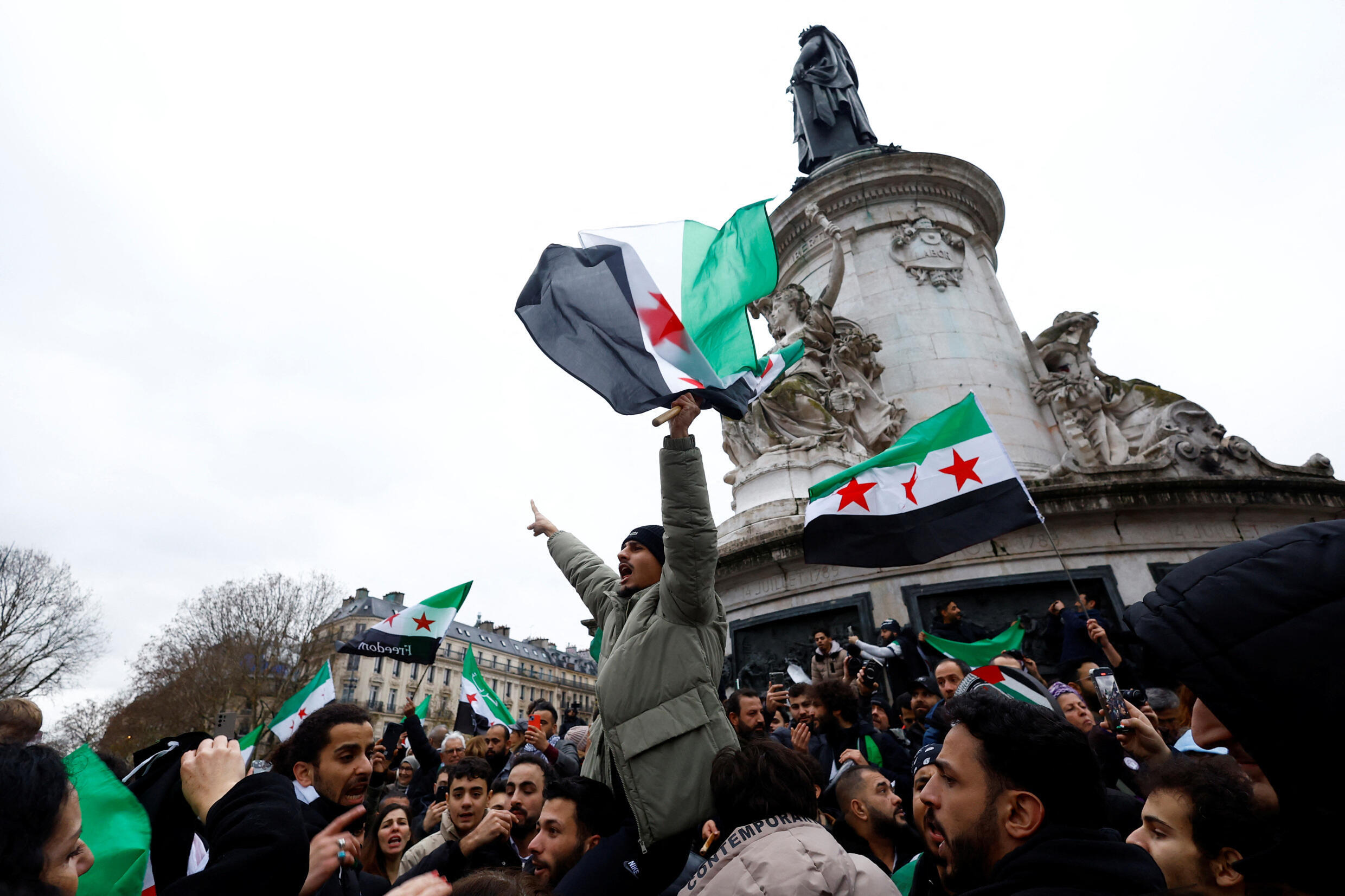 Les gens brandissent des drapeaux de l'opposition syrienne alors qu'ils célèbrent sur la place de la République, après que les rebelles syriens ont annoncé qu'ils ont évincé le président Bashar al-Assad, à Paris, France, le 8 décembre 2024.
