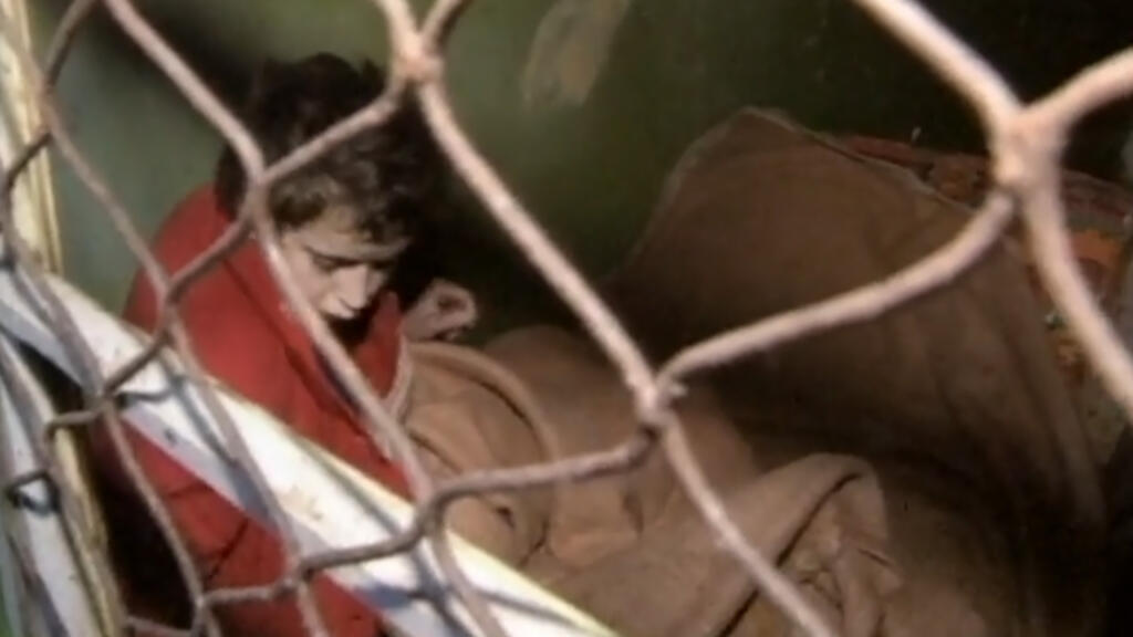 Un copil încuiat într-o celulă cu o ușă din plasă metalică, într-un orfelinat