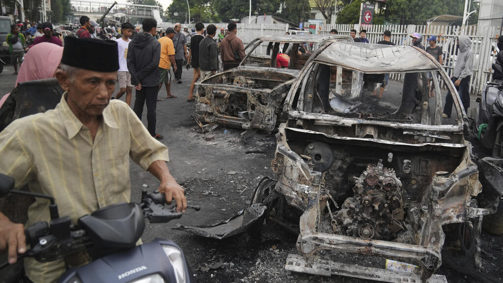 A man rides his scooter past the wreckages of cars burned during violent protests against lawmakers' allowance and alleged police brutality after a delivery rider was run over by a police armored vehi
