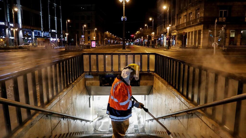 Un travailleur portant une combinaison de protection nettoie et désinfecte un escalier d'un passage souterrain pour empêcher la propagation du Covid-19, au centre-ville de Budapest, le 26 mars 2020..