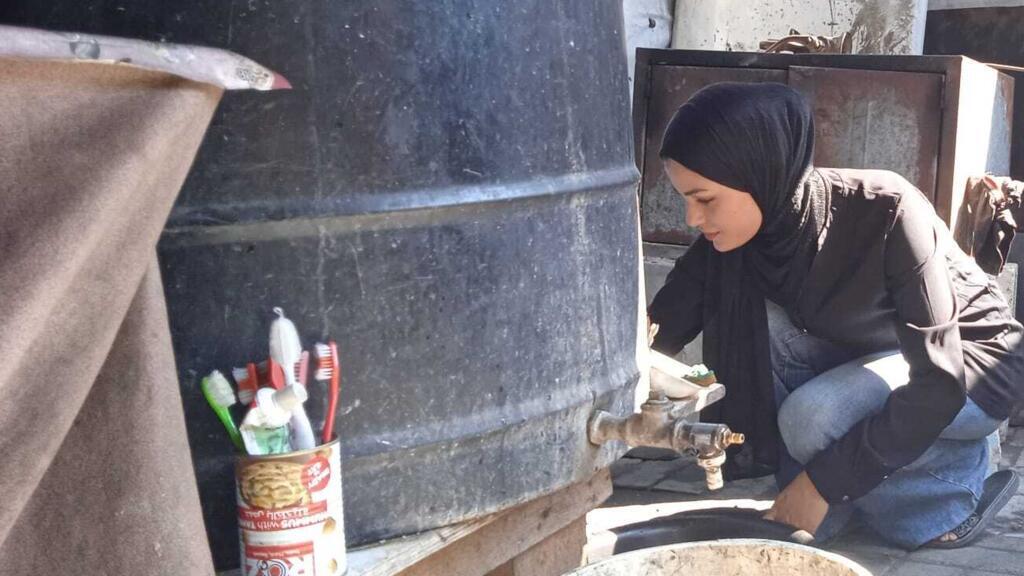 Bayan, dans la tente de sa famille, en train de nettoyer des ustensiles de cuisine, en juillet 2025.