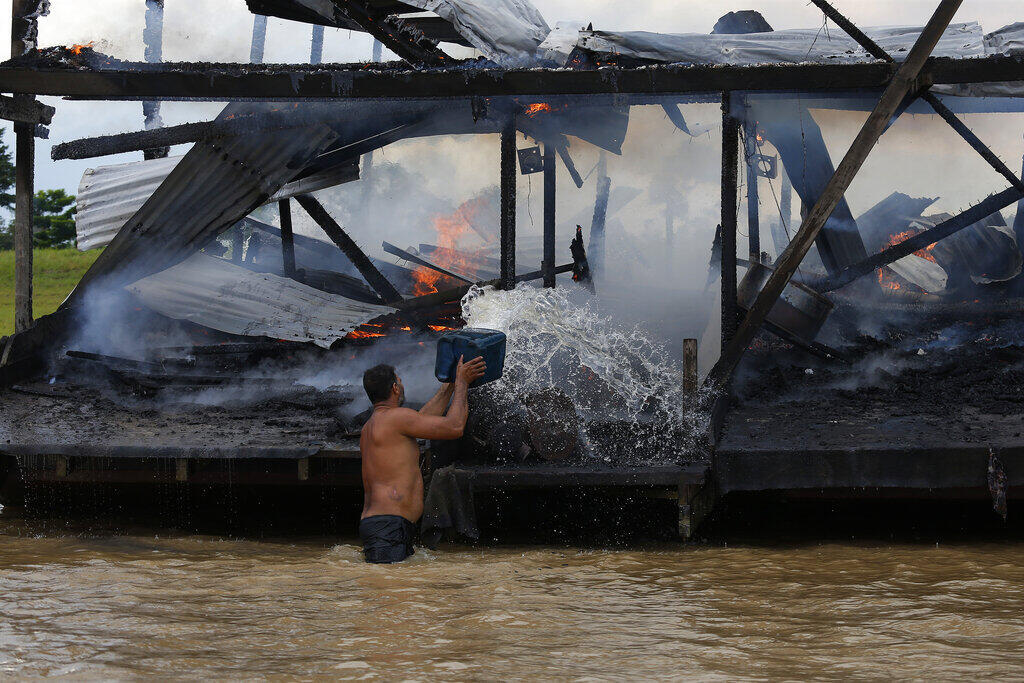 Um garimpeiro ilegal joga água em uma das mais de 60 barcas de dragagem que foram incendiadas por oficiais do Instituto Brasileiro do Meio Ambiente e dos Recursos Naturais Renováveis, IBAMA, durante uma operação para tentar conter a mineração ilegal de ouro no rio Madeira, um afluente do rio Amazonas em Borba, estado do Amazonas. (28/11/2021)