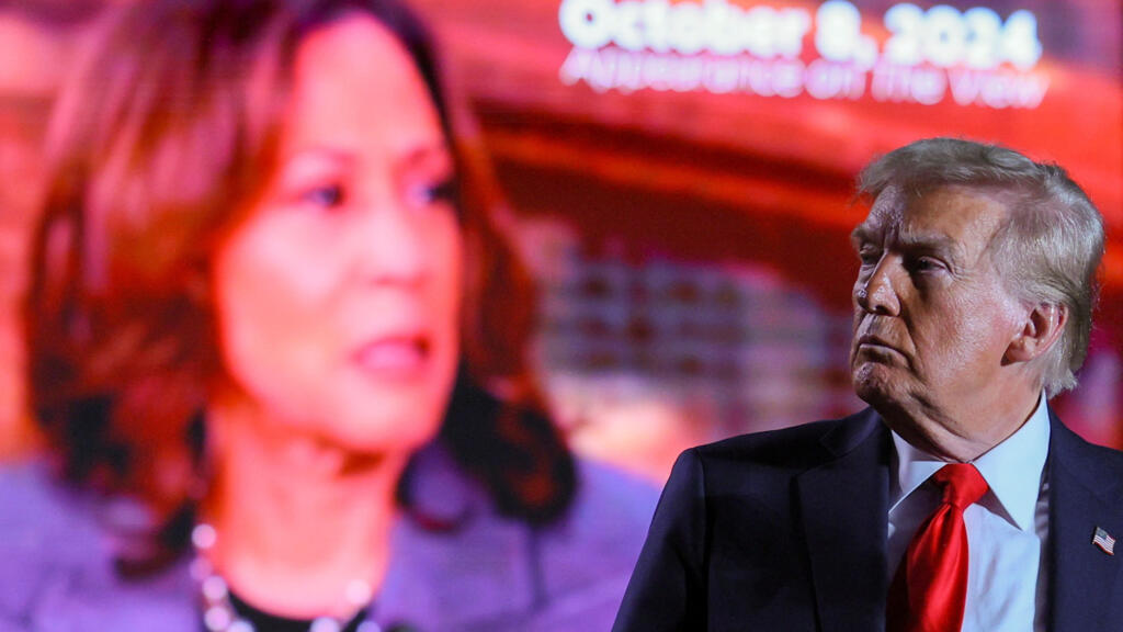 Republican presidential nominee and former US President Donald Trump (R) looks on as a screen shows Democratic presidential nominee and US Vice President Kamala Harris during a campaign rally, 1 November 2024.