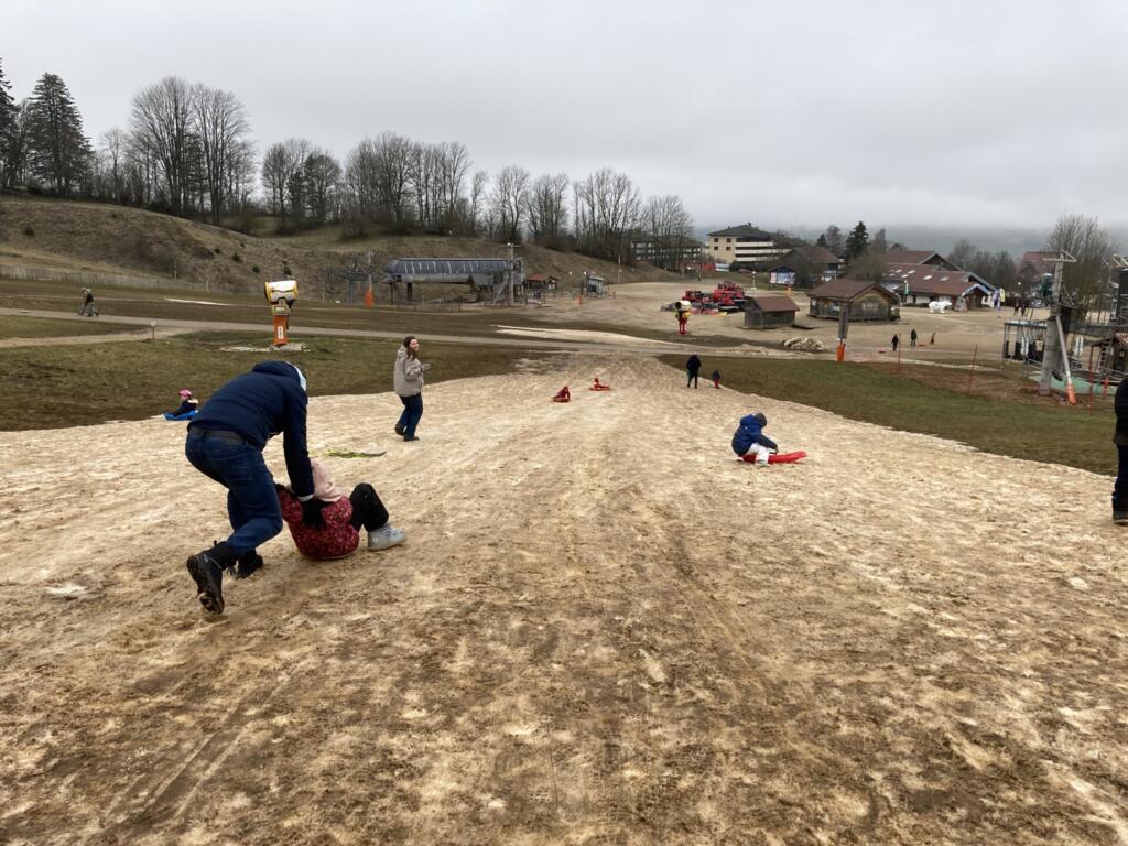 Sur le peu de neige qu'il reste et se mélange à la terre, des familles font de la luge. Métabief, le 4 mars 2024.