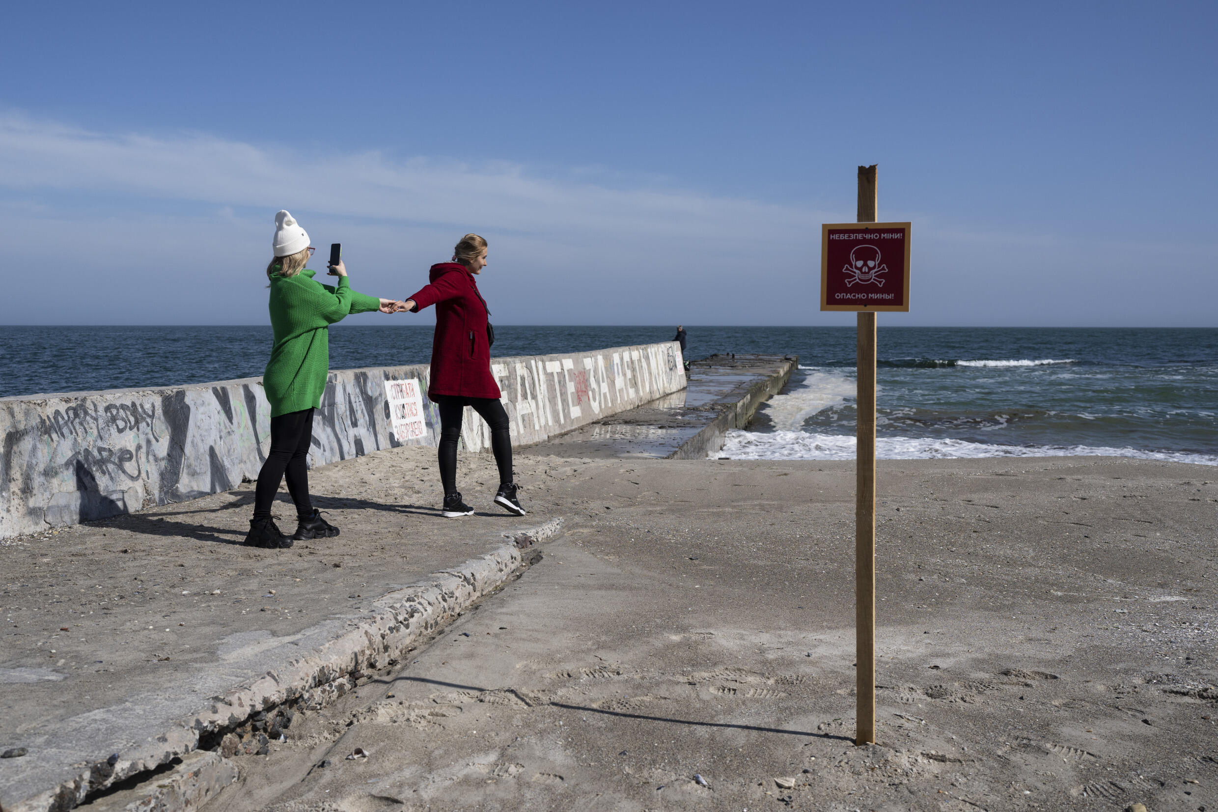 A Odessa, deux amies se prennent en photo face à la mer et à côté d'un panneau indiquant : "Danger, mines", le 8 avril 2022.