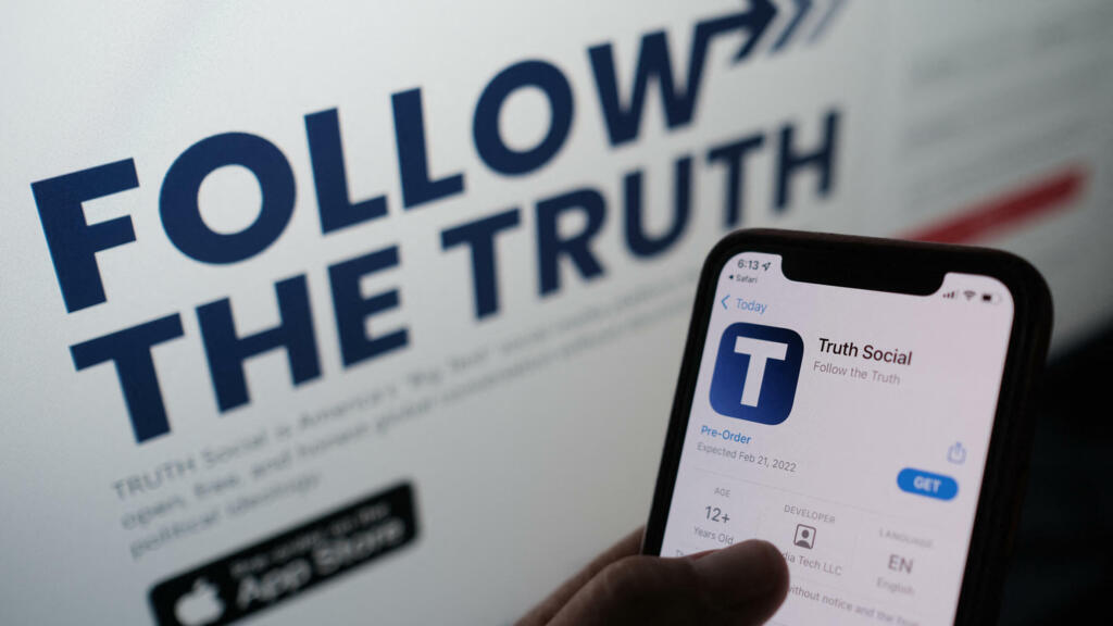 Foto ilustrativa mostra uma pessoa verificando a loja de aplicativos em um smartphone para "Truth Social", com seu website em uma tela de computador ao fundo, em Los Angeles, 20 de outubro de 2021.