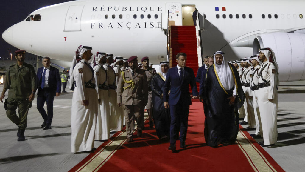 Le président français Emmanuel Macron, accueilli par des responsables du ministère des Affaires étrangères à son arrivée à l'aéroport de Doha, pour une visite d'une journée au Qatar, le samedi 2 décembre 2023.