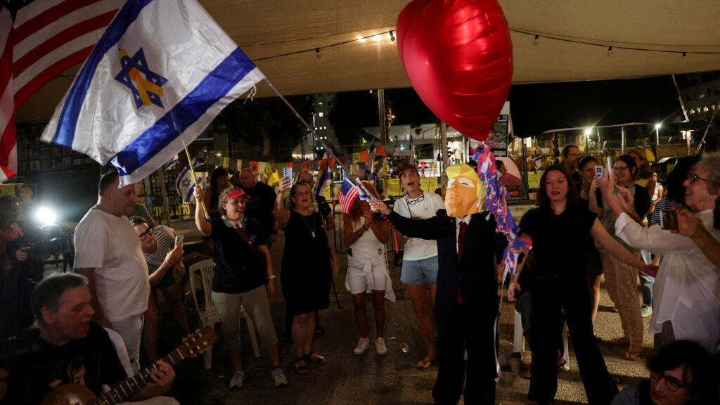 Une personne portant un masque à l'effigie du président américain Donald Trump agite un drapeau israélien orné d'un ruban jaune au centre, alors que la foule célèbre l'annonce par Donald Trump d'un accord entre Israël et le Hamas sur la première phase d'un cessez-le-feu à Gaza, sur la « place des otages », à Tel Aviv, en Israël, le 9 octobre 2025.