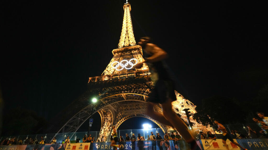 Des spectateurs se tiennent au pied de la tour Eiffel alors qu'ils regardent les coureurs participer au Marathon pour tous, aux Jeux olympiques d'été de 2024, à Paris, le 10 août 2024.
