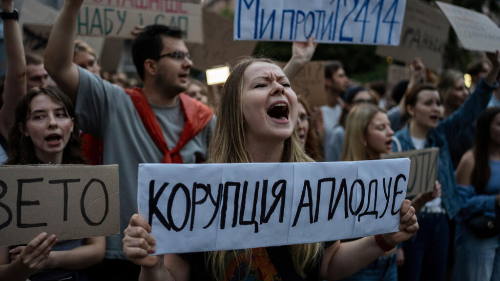 Une manifestante tient une pancarte sur laquelle on peut lire « La corruption applaudit » lors d'une manifestation contre une loi visant les institutions anti-corruption, dans le centre de Kiev, en Ukraine, le mardi 22 juillet 2025.