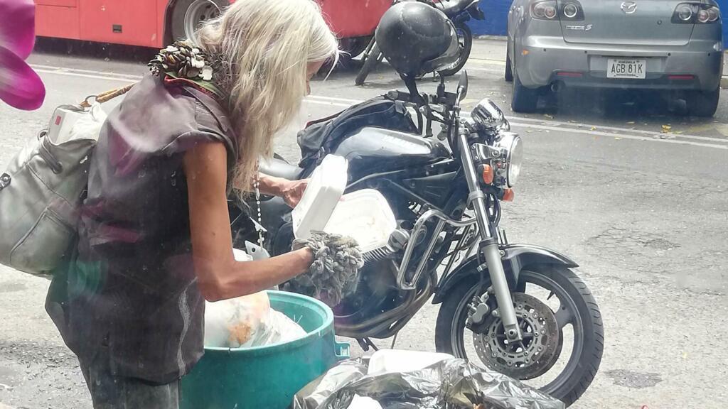 Idosa revira lixo em Caracas à procura de alimentos.