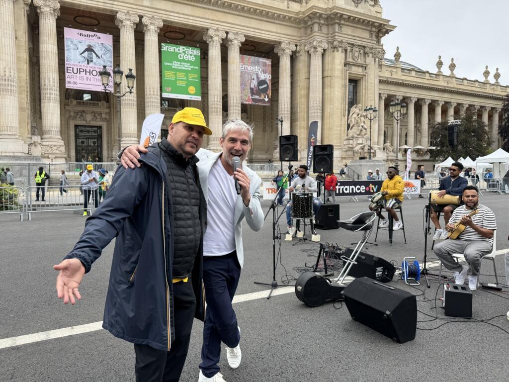 O diretor do Carnaval Tropical de Paris, Joby Garnier, posa ao lado do grupo de samba que se apresentou em frente ao Grand Palais, no centro de Paris, neste domingo, 6 de julho.