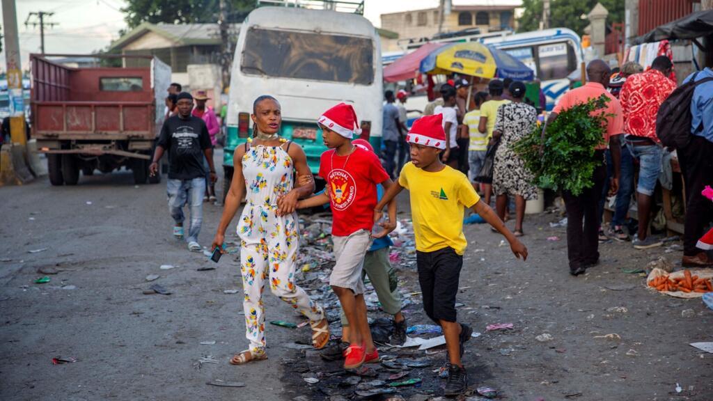 Une femme marche avec ses garçons dans une rue tout en portant des bonnets de Noël à Port-au-Prince, en Haïti, jeudi 24 décembre 2021.