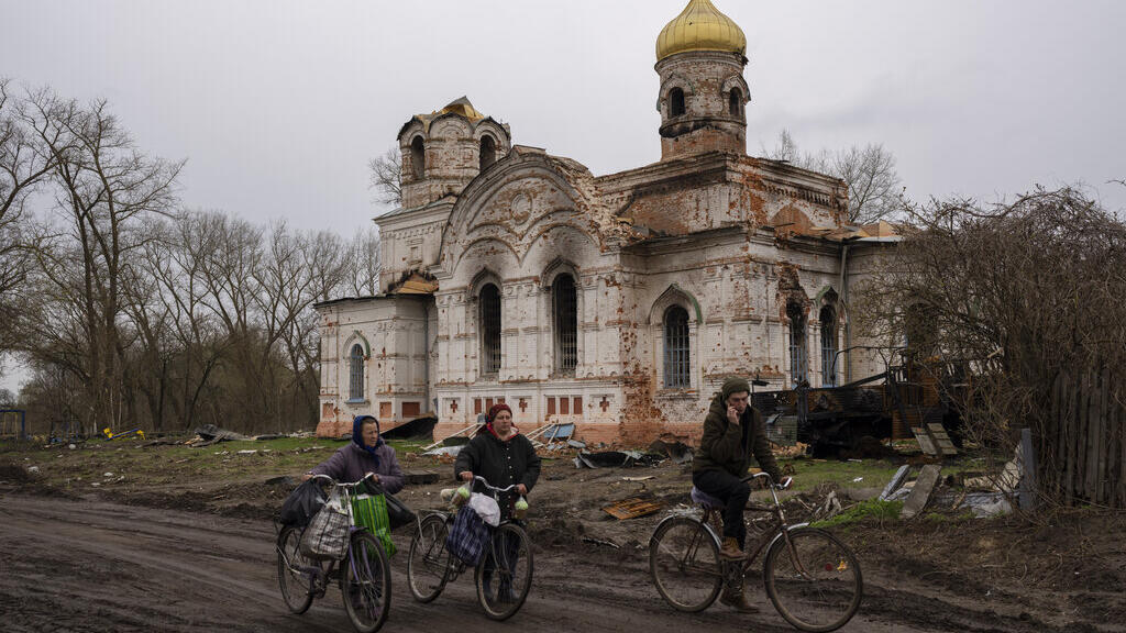 Des Ukrainiens marchent avec leur vélo devant une église endommagée, à Lukashivka, dans le nord de l'Ukraine, vendredi 22 avril 2022.