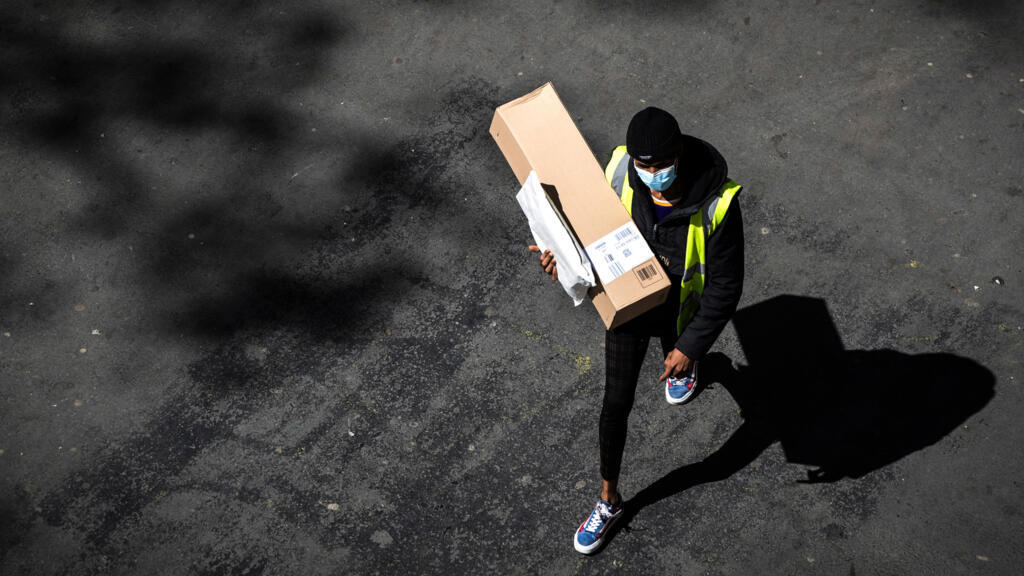 Un livreur masqué porte un colis Amazon et une enveloppe dans les rues de Paris, le 15 avril 2020, au 30e jour du confinement.
