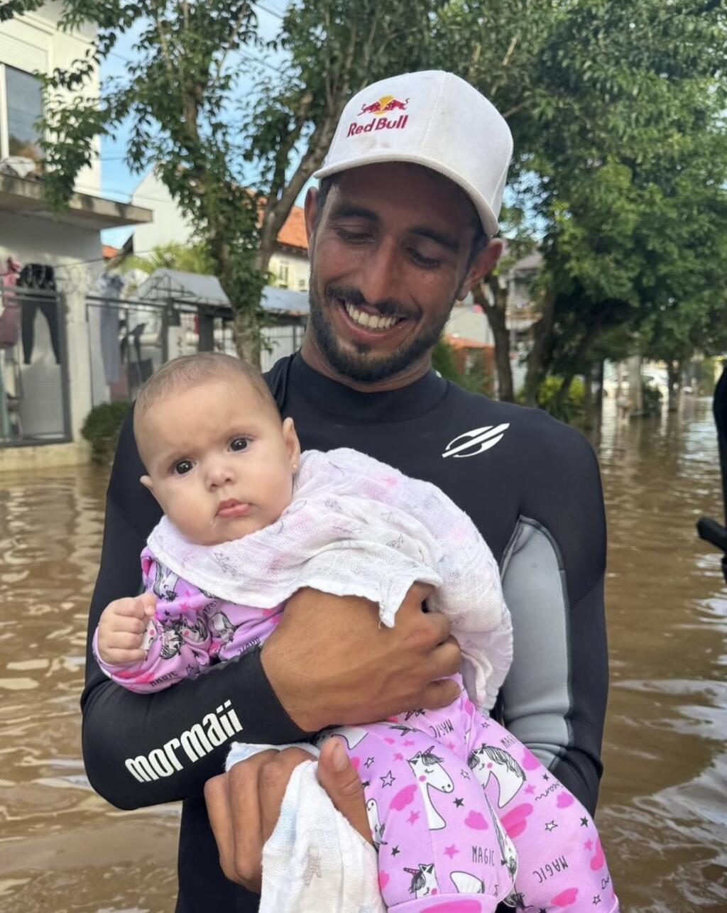 O surfista Lucas Chumbo segura um bebê que resgatou durante as operações de salvamento no Rio Grande do Sul.
