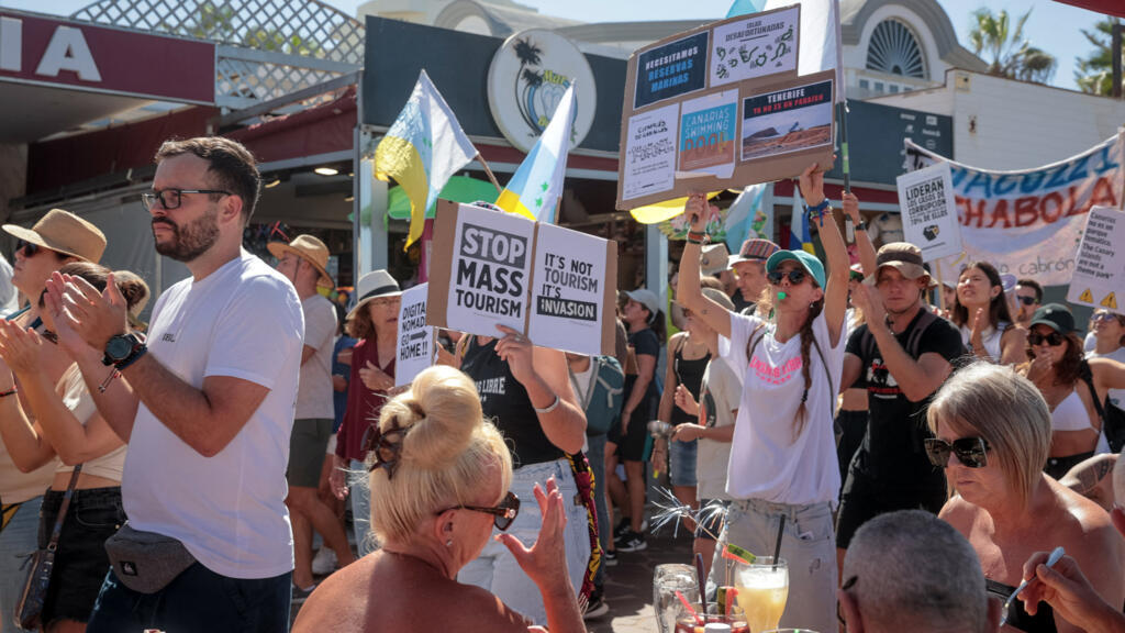 Manifestantes fazem passeata durante manifestação contra o turismo de massa enquanto turistas sentam-se em um terraço, em Arona, na ilha canária espanhola de Tenerife, em 20 de outubro de 2024.