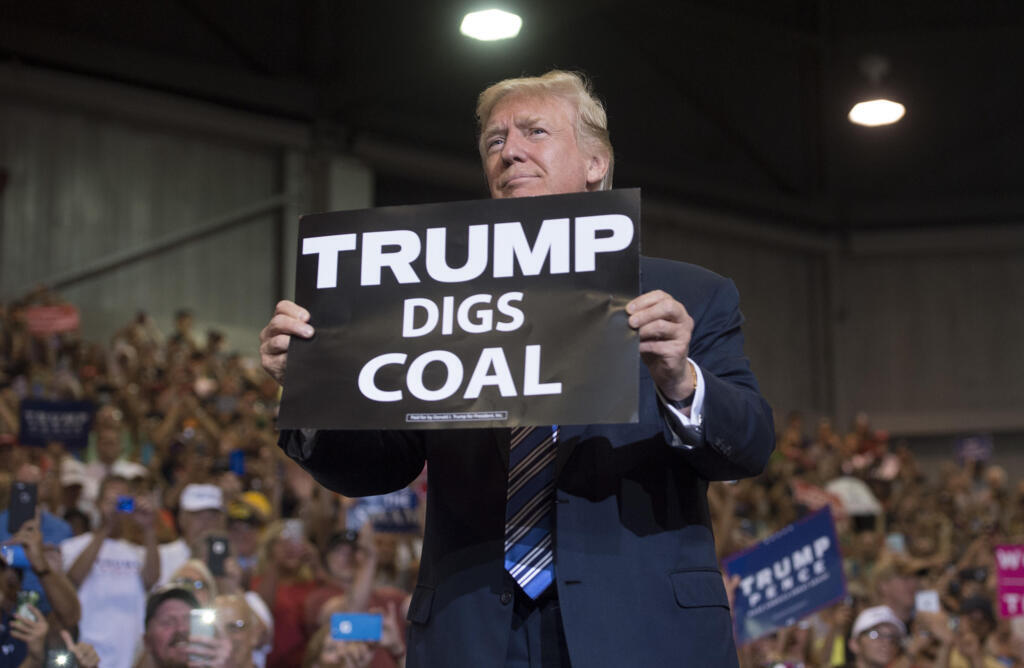 O Presidente dos EUA, Donald Trump, com uma placa "Trump Digs Coal" durante comício em Huntington, Virgínia Ocidental, 3/08/2017. Durante a campanha presidencial de 2016 nos EUA, Donald Trump não hesitou em colocar um capacete na cabeça e fazer campanha pelo carvão em locais de minas ameaçadas. Estas se setem sob ameaça devido a competitividade do gás xisto e pelas regulamentações ambientais estabelecidas pela administração Obama para adequar o país ao Acordo de Paris.