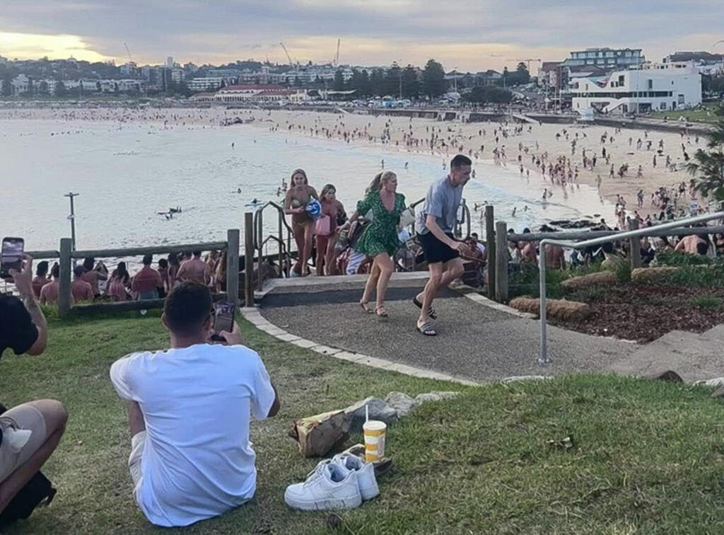 Cette capture d'écran d'une vidéo UGC prise le 14 décembre 2025 et fournie par Mike Ortiz montre la foule présente à la plage de Bondi, ainsi que des baigneurs fuyant après que des hommes armés ont ouvert le feu, à Sydney, le 14 décembre 2025.