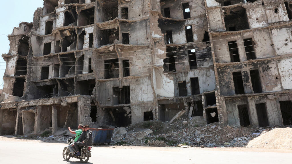 People ride a motorbike past a damaged building in Aleppo as US President Donald Trump announced that he would order the lifting of sanctions on Syria, 14 May.
