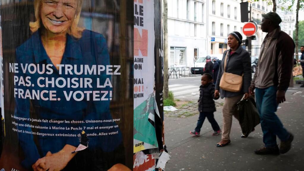 People pass a poster depicting French presidential election candidate for the far-right Front National (FN) Marine Le Pen with the face of U.S. President Donald Trump in 2017.