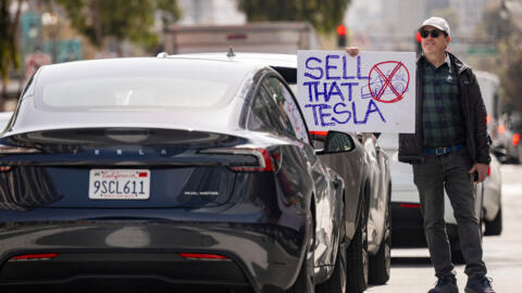 Un manifestant tient une pancarte sur laquelle on peut lire «Vends cette Tesla» devant un conducteur de Tesla lors d'un rassemblement devant un concessionnaire de la marque à San Francisco, samedi 15 mars 2025.