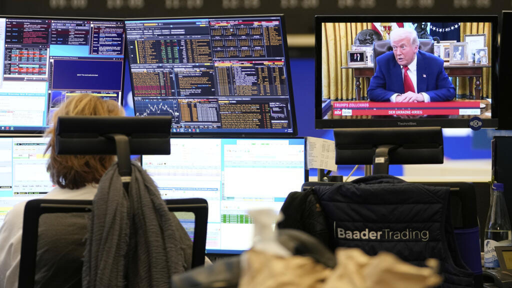 A trader sits in front of computer screens on the trading floor of the Frankfurt Stock Exchange beside a TV showing U.S. President Donald Trump on a news channel in Frankfurt, Germany, the day after T
