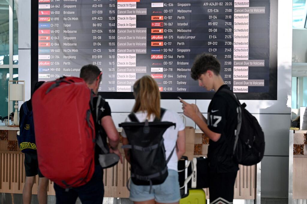 Passageiros observam um painel eletrônico exibindo voos cancelados após a erupção do vulcão Lewotobi Laki-Laki, no Aeroporto Internacional Ngurah Rai, em Tuban, perto de Denpasar, na ilha turística de Bali, na Indonésia, em 18 de junho de 2025.  (Foto de SONNY TUMBELAKA / AFP)
