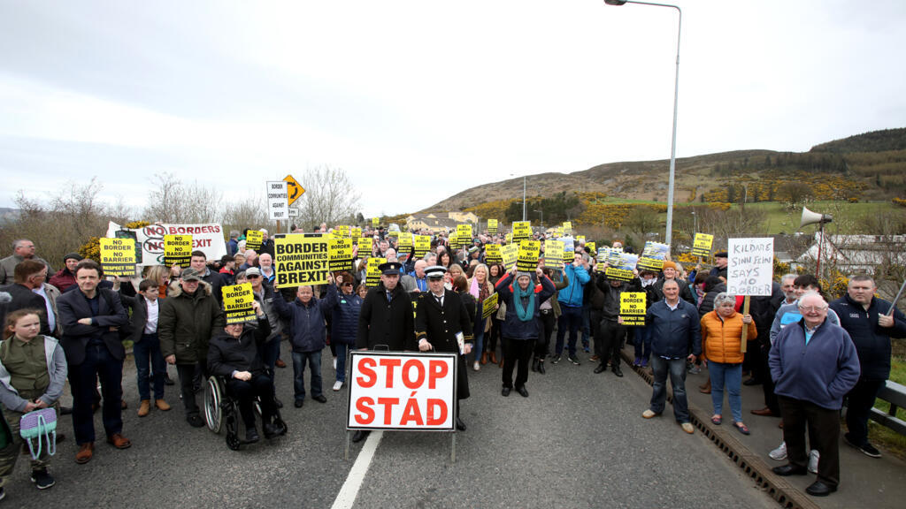Les manifestants contre toute frontière entre l'Irlande et l'Irlande du Nord à cause du Brexit tiennent des pancartes à la frontière de Carrickcarnan entre Newry (Irlande du Nord) et Dundalk (République irlandaise) le 30 mars 2019.