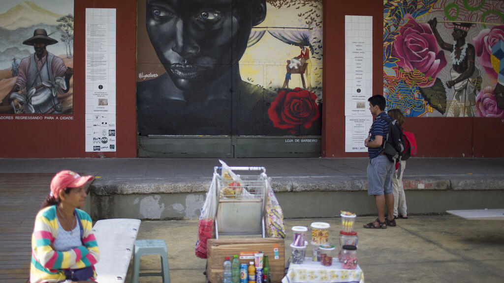 Mulher vende bebidas e doces em frente à fachada do Museu do Amanhã, no Rio de Janeiro. Desde os tempos coloniais, o comércio informal foi atividade econômica de camaas vulneráveis da população (AP Photo/Renata Brito)