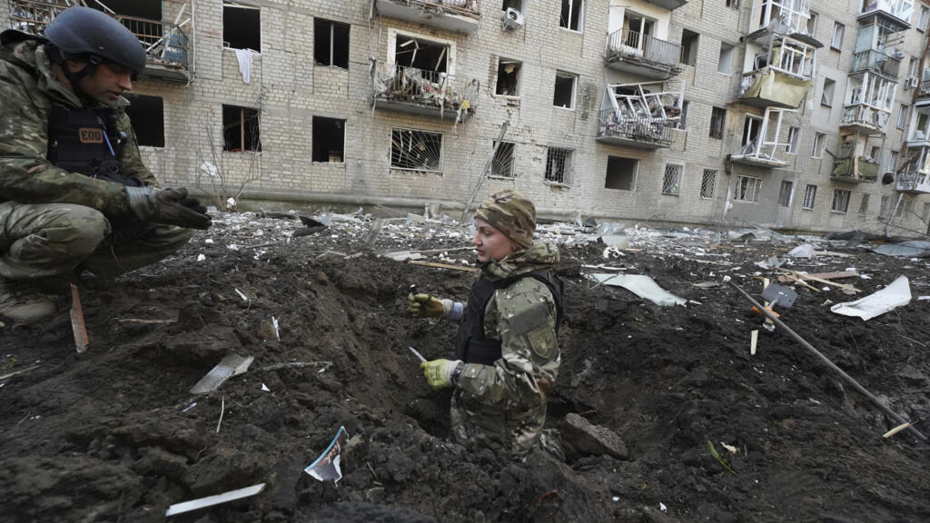 Des policiers inspectent un cratère devant un immeuble résidentiel endommagé par une frappe russe à Kharkiv, en Ukraine, le 27 mars 2024.