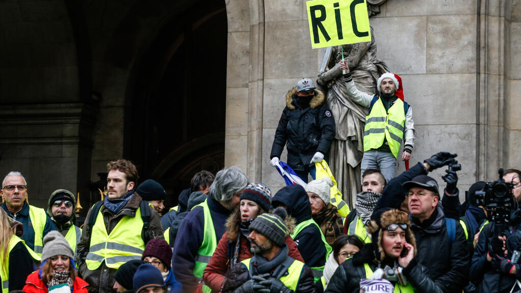 Un gilet jaune tient un carton portant l'inscription «référendum d’initiative citoyenne - RIC» lors d'une manifestation contre la hausse du coût de la vie, devant l'Opéra de Paris, le 15 décembre 2018.