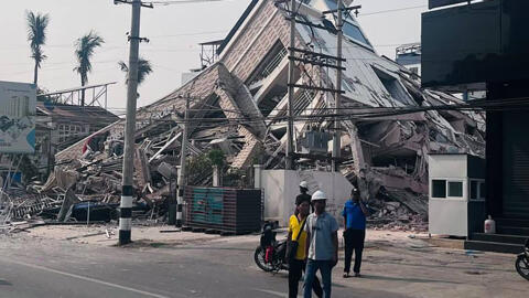 Des secouristes se tiennent devant un immeuble effondré, le 28 mars 2025, à Mandalay (Birmanie).