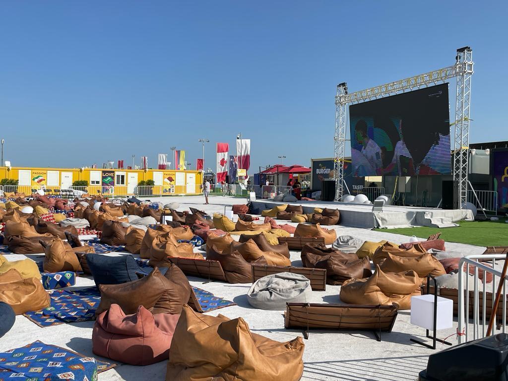 Um grande espaço com poltronas e pufes ao ar livre para os torcedores assistirem juntos a partidas em um imenso telão.