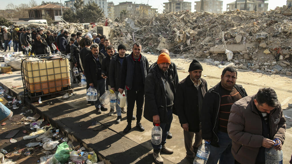 People line up for water by collapsed buildings in Kahramanmaras in southern Turkey.