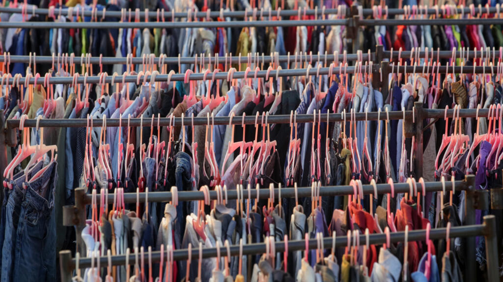 Sélection de différents vêtements usagés pour hommes, femmes et enfants sur le rack dans un magasin d’occasion.