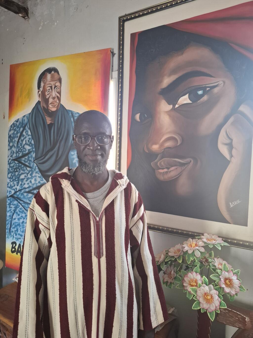 Alioune Badara Ndoye devant certaines de ses peintures.