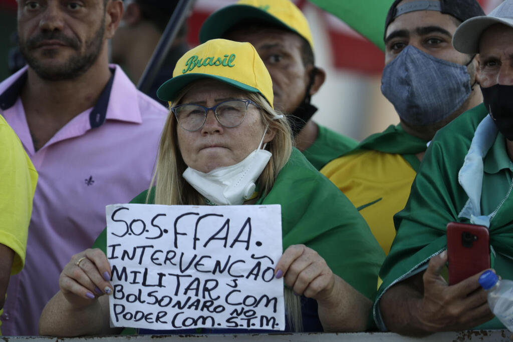 Um manifestante segura uma placa em português que diz "Forças Armadas SOS. Intervenção militar com Bolsonaro no poder" durante uma manifestação em apoio ao presidente brasileiro Jair Bolsonaro em frente ao palácio presidencial do Planalto em Brasília, Brasil, na segunda-feira, 29 de março de 2021.