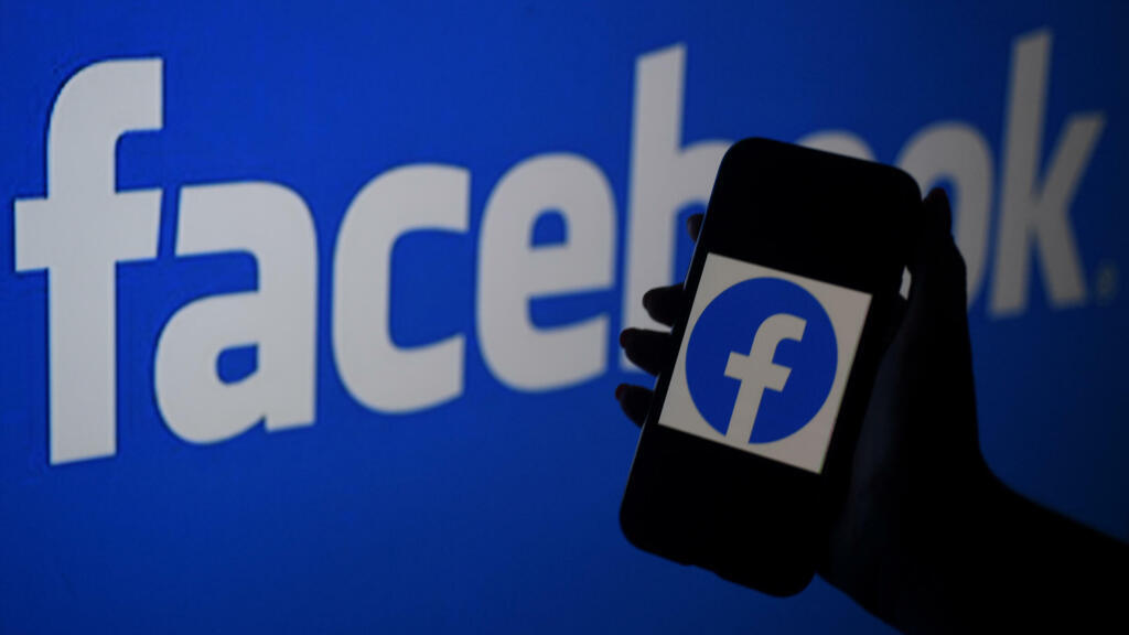 A smart phone screen displays the logo of Facebook on a Facebook website background
