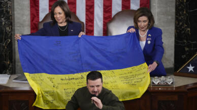 La vice-présidente américaine et cheffe du Sénat Kamala Harris et la cheffe de la chambre des représentants Nancy Pelosi tiennent un drapeau signé par des soldats ukrainiens apporté comme cadeau par le président ukrainien Volodymyr Zelensky, lors de sa visite à Washington le 21 décembre 2022.