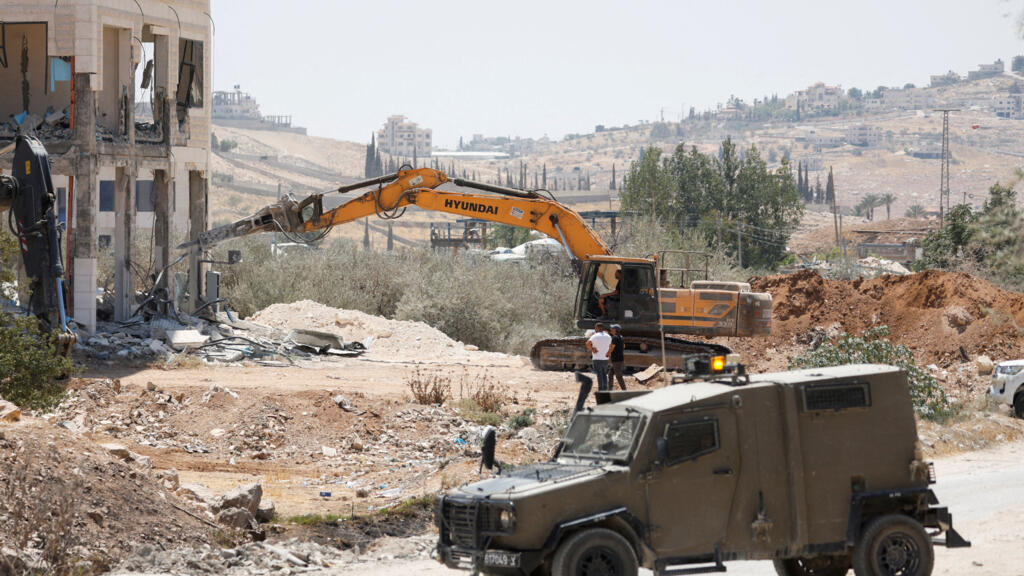 An Israeli military vehicle is parked near Israeli heavy machinery demolishing a Palestinian building near Bethlehem in the Israeli-occupied West Bank August 6,2025.