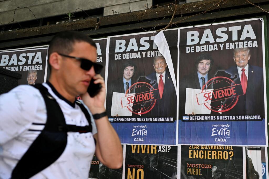 Un homme passe devant une affiche représentant le président argentin Javier Milei et le président américain Donald Trump, sur laquelle on peut lire « Plus de dette et de reddition », à Buenos Aires le 14 octobre 2025. Le président argentin en difficulté Javier Milei s'est rendu à Washington, misant sur une démonstration très médiatisée de soutien politique et économique de la part du président allié Donald Trump avant les élections législatives cruciales.