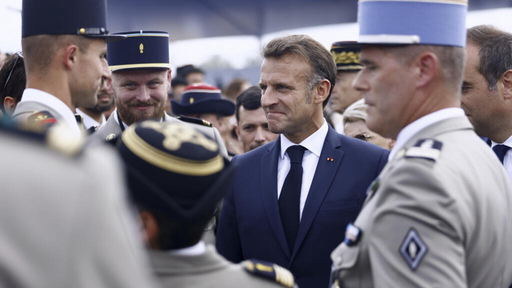 Le président français Emmanuel Macron est entouré de responsables militaires alors qu'il quitte le défilé militaire du 14 juillet sur l'avenue des Champs-Élysées, le lundi 14 juillet 2025.