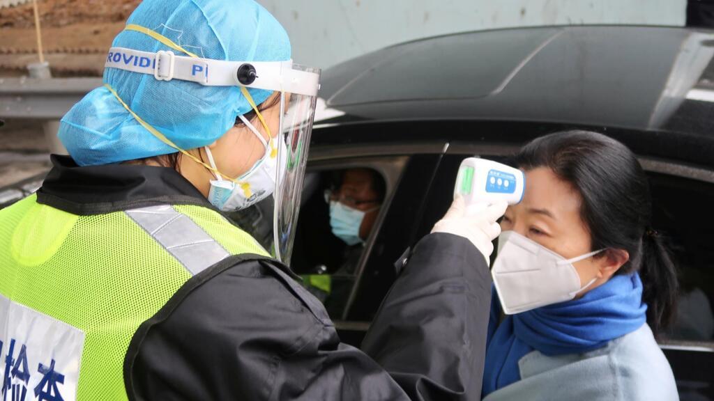 Officier de la sécurité chinoise prenant la température de la passagère d'un véhicule, à Xianning, non loin de Wuhan, le 24 janvier 2020.
