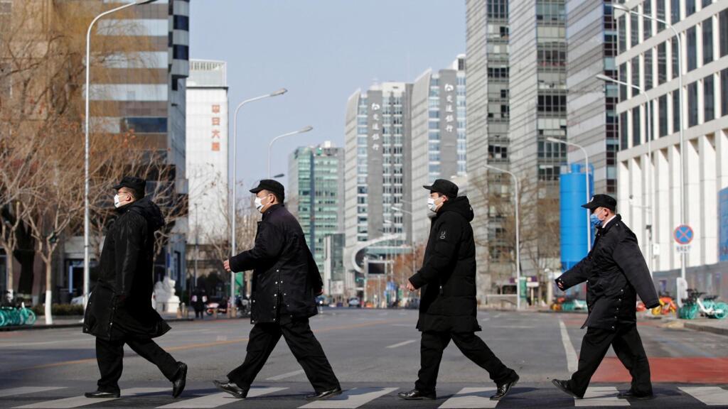 Des membres du personnel de sécurité portant des masques traversent une rue de Financial Street dans le centre de Pékin, le 3 février 2020.