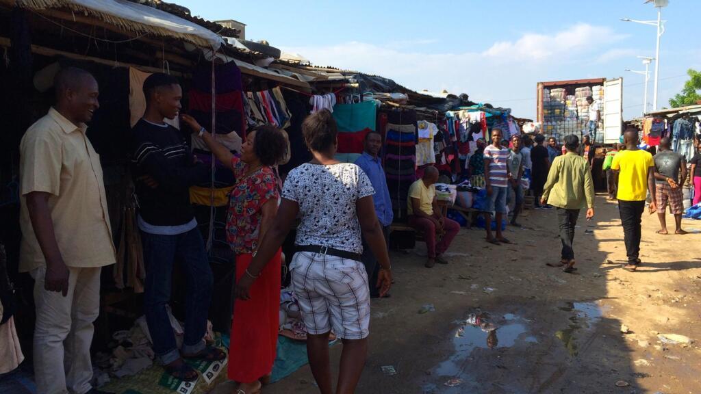 Ogwo Orgi Ogwo, vendeur de fripes au marché Missèbo à Cotonou, avec un de ses fils. Au fond, un camion rempli de ballots est déchargé. 