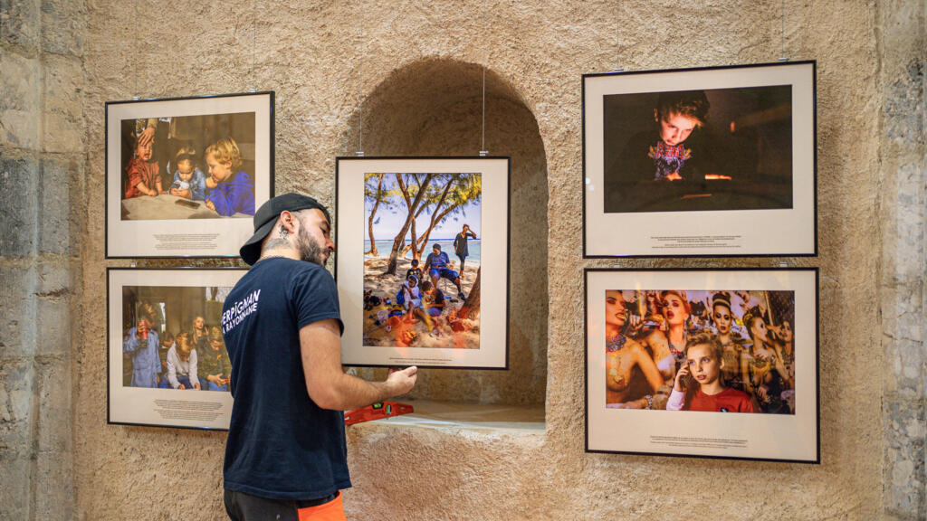 Un employé installe des photographies de l'exposition « Grandir dans la cour d'écrans » de Jérôme Gence lors de la 36e édition du festival de photographie de presse « Visa pour l'image » à Perpignan, dans le sud-ouest de la France, le 28 août 2024.
